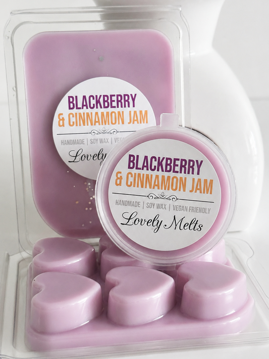 A clear plastic clamshell package of wax melts with a heart-shaped wax insert, alongside a smaller round tub of the same product. Both have white labels reading 'BLACKBERRY & CINNAMON JAM' and 'Lovely Melts.