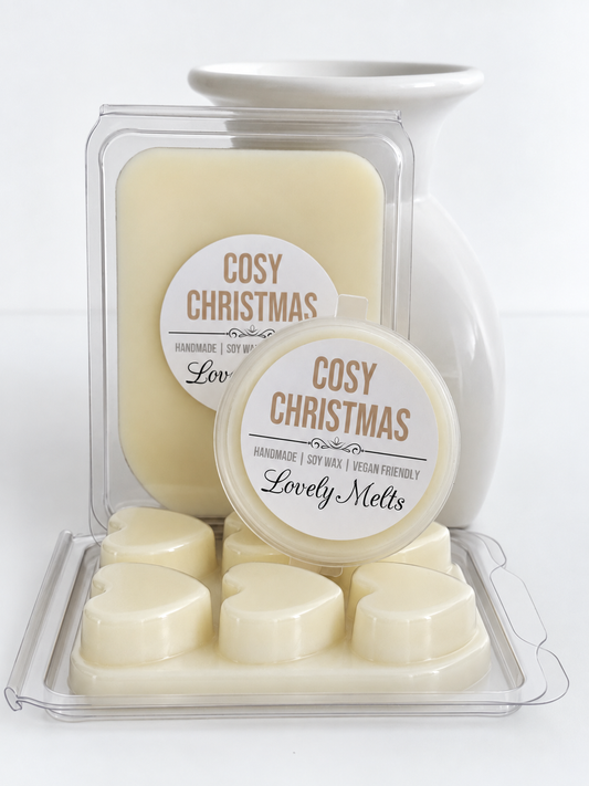 Cream-colored handmade soy wax melts in heart-shaped and round wax melts, packaged in clear clamshell containers with white labels reading 'COSY CHRISTMAS' and 'Lovely Melts', set against a white ceramic vase on a white background.