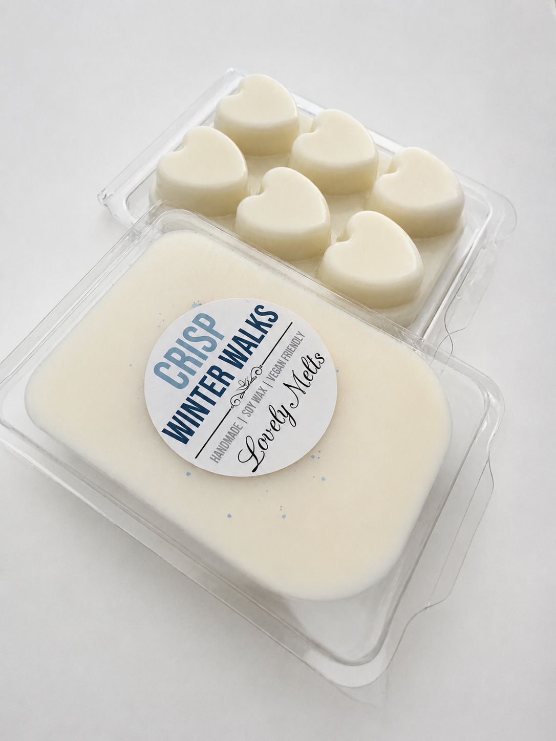A package of 'Crisp Winter Walks' hand-poured wax melts by Lovely Melts, featuring a large rectangular bar of creamy off-white wax in the foreground and six small heart-shaped wax melts arranged in a clear tray behind it.
