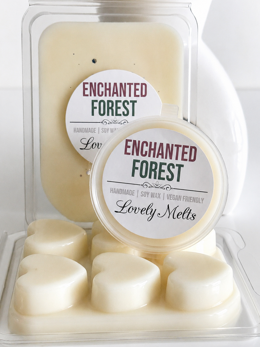Two clear plastic containers of Enchanted Forest scented melts by Lovely Melts, one larger wax melt block and one smaller round wax melt tray with several heart-shaped wax melts, set against a white ceramic vase background.