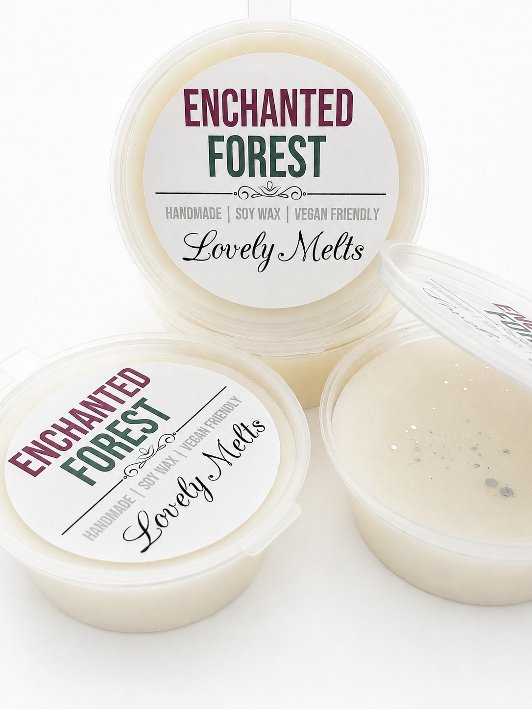 Three round plastic jars of Enchanted Forest soy wax melts by Lovely Melts on a white background, with one open pot showing the creamy wax inside.