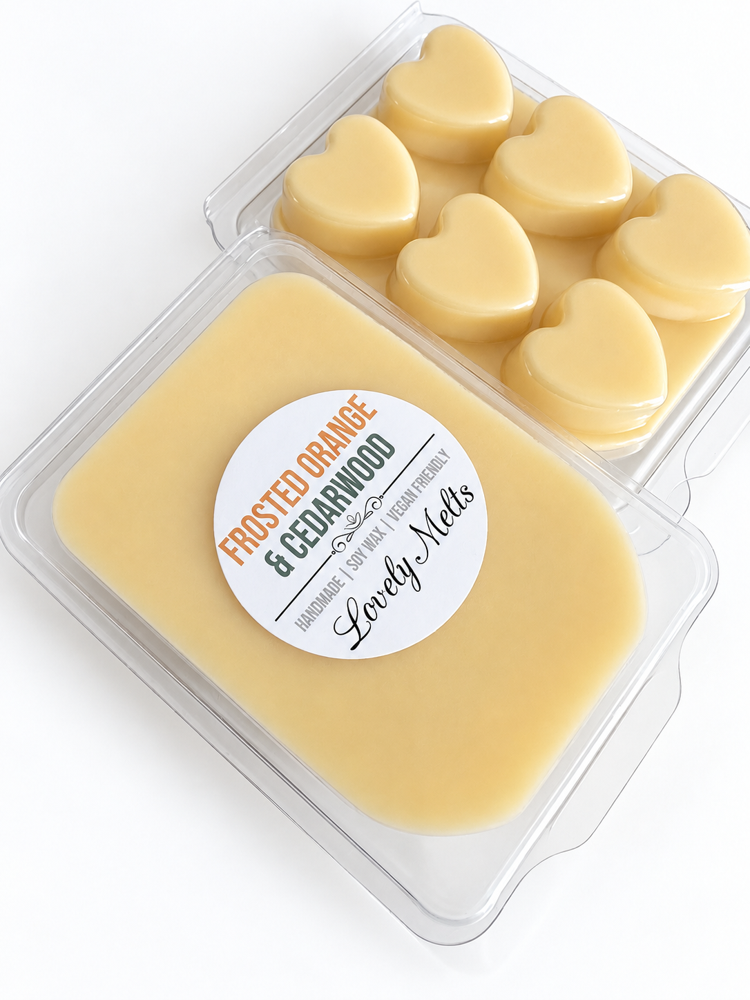 Two clear clamshell packages of heart shaped wax melts on a white background. The front package contains pale orange wax melts with a round white label reading 'FROSTED ORANGE & CEDARWOOD' and 'Handmade Wax Melts' by Lovely Melts.