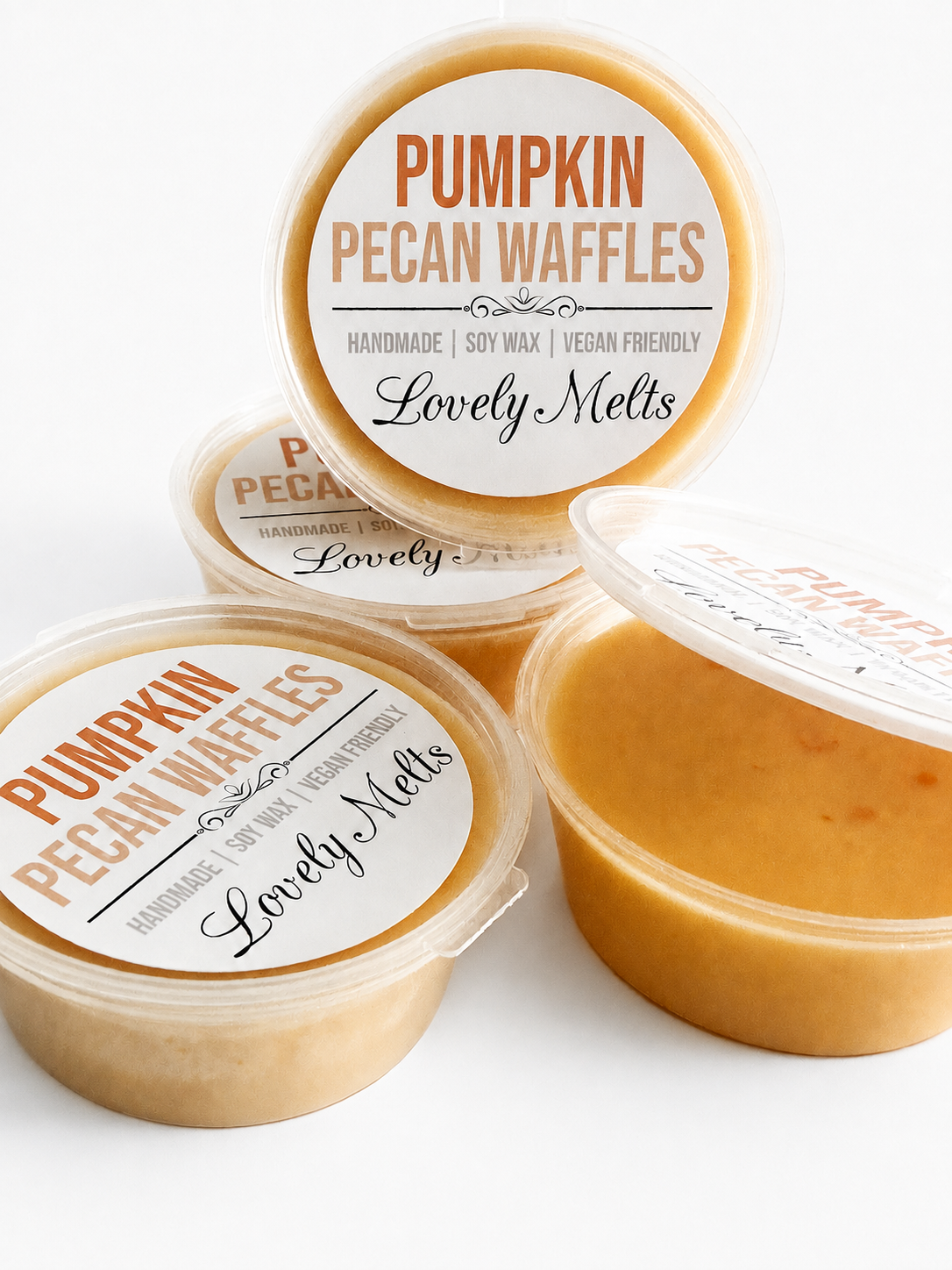 Three round plastic tubs of pumpkin pecan waffles on a clean white background, with one tub open to show the warm golden-orange wax melt inside. The labels read 'Pumpkin Pecan Waffles' and 'Lovely Melts'.