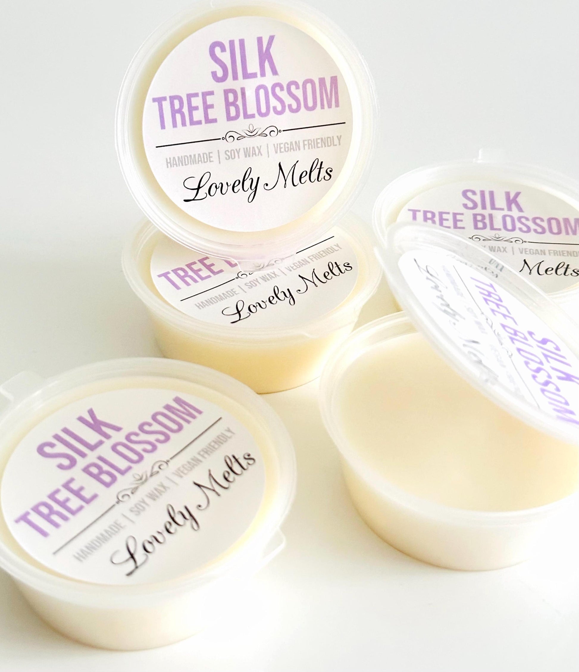 Four small round plastic containers of Lovely Melts Silk Tree Blossom handcrafted soy wax melts on a clean white background, with one container open to show the pale cream wax inside.