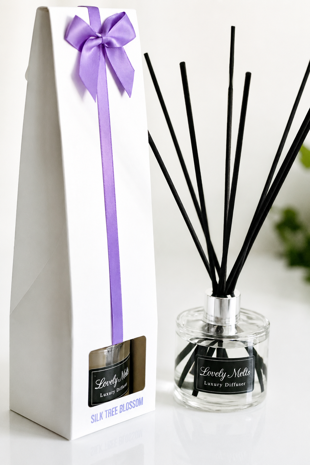 Reed diffuser set with black sticks and a glass container, accompanied by a white box with a purple bow.
