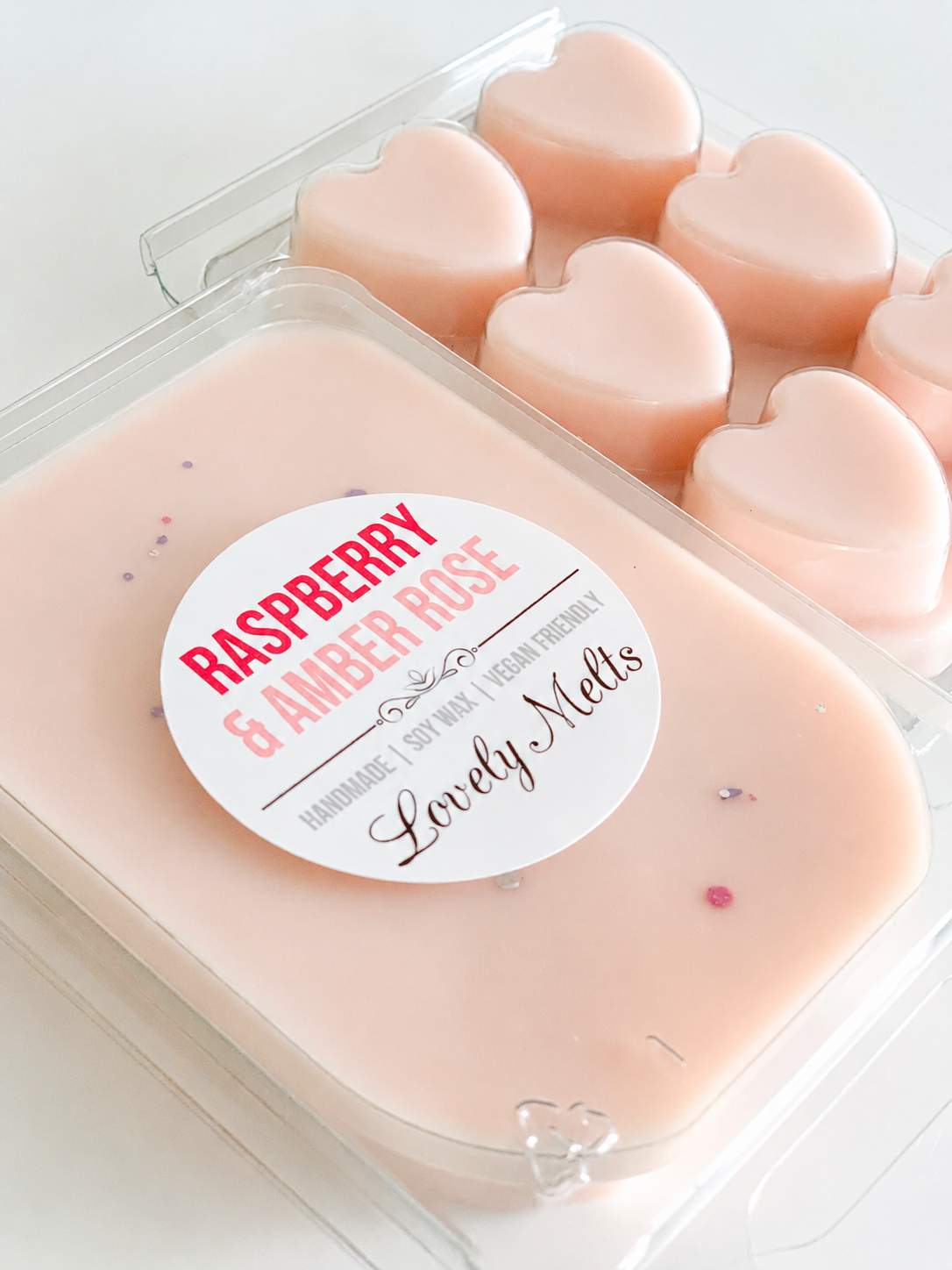 Heart-shaped raspberry rose scented wax melts in a clear container with a label.